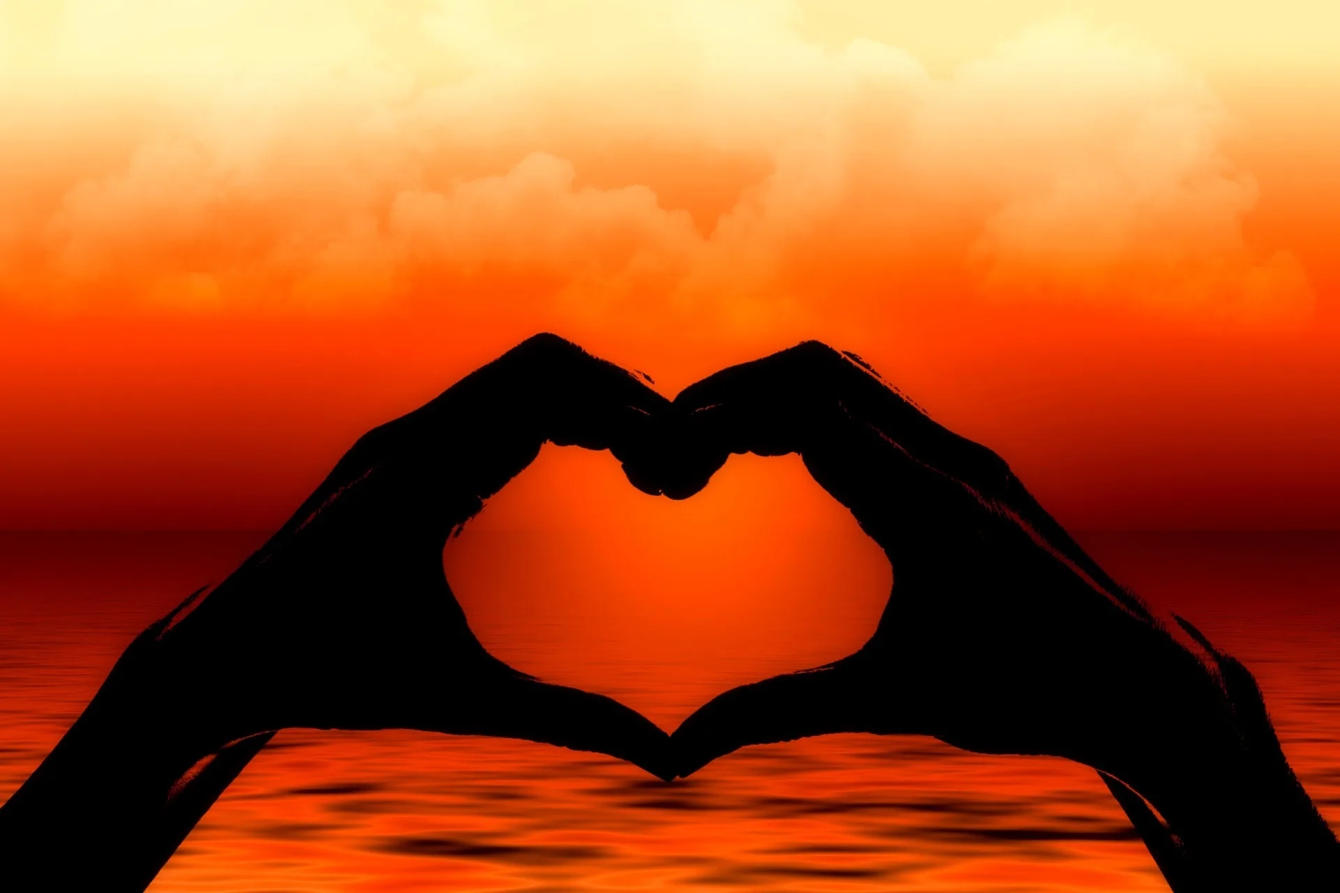 Silhouette hands forming a heart shape at sunset over the ocean